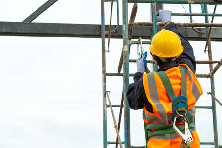 A worker working at height equipment. Fall arrestor device for worker with hooks for safety body harness on selective focus. Worker as in construction background.の写真素材