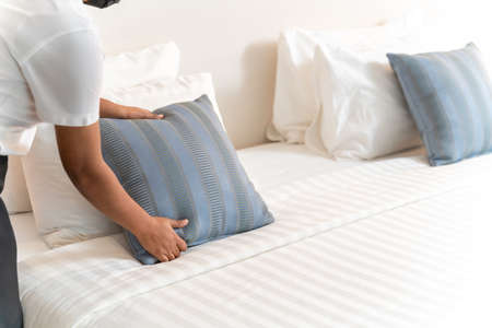 close up hand of maid setting up pillow on bed sheet in hotel room