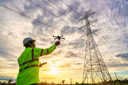 Asian engineers are launching drones to inspect the power station for a planned work by generating electricity from a high-voltage transmission tower at sunset.の写真素材