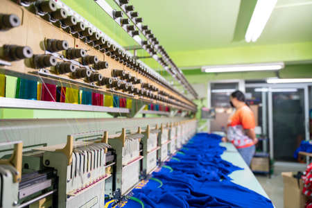 A worker stands in control of a sewing machine. Embroidery area in textile factory in industrial zone with modern machinery and technology systems. select focus of sewing machine.の写真素材