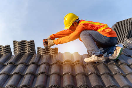 Asian Roofer working on roof structure of building on construction site,Roofer using air or pneumatic nail gun and installing Concrete Roof Tiles on top new roof.の写真素材