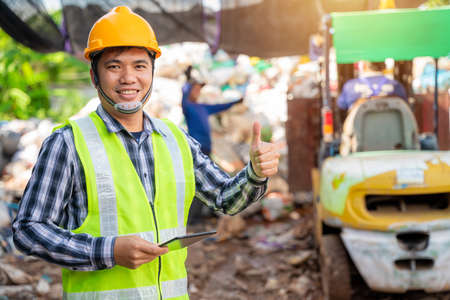 Asian  foreman thumbs up and holding tablet and looking at recycle waste factory with a forklift on the background.の写真素材