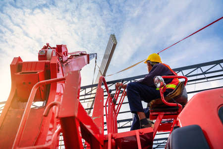 Asian Crane driver, Crane driver sit a top in a mobile crane cabin and working lifting the roof or PU foam roof sheet at the construction site.の写真素材