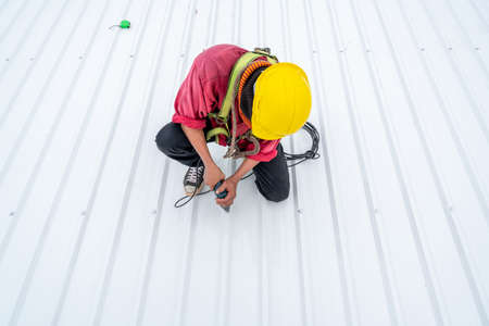 A Roofer worker using electric drill nail gun and installing PU foam roof sheet on top of the new roof, Concept of residential building under construction.の写真素材