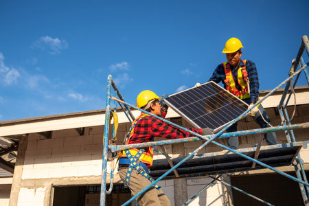 Asian technicians or workers wearing fall protection safety clothing carry solar cells to install on the roof of a house. Concept of alternative and renewable energy.の写真素材