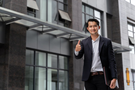 Asian business man looking at the camera and giving a thumbs up in urban public space.