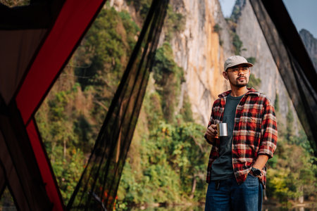 Asian man standing in front of a tent holding a hot drink mug. coffee and camping.の写真素材