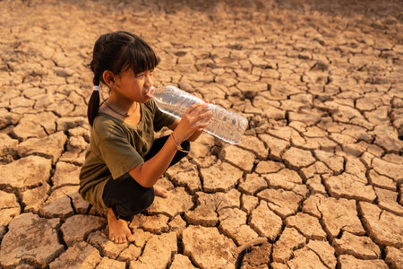 Asian girl with drought sitting drinking clean water on dry ground. Concept drought and crisis environment.の写真素材