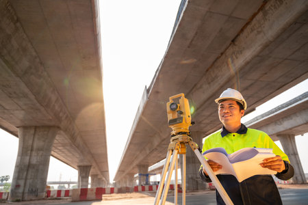 A male civil engineer or surveyor standing holding a blueprint with a happy smile at road construction site, Surveyor equipment. Highway.の写真素材
