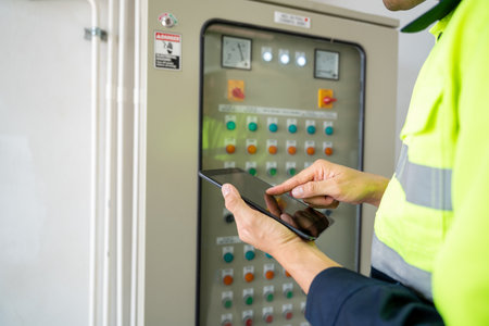 Close up hand of An engineer or electrician working on electrical check of water supply system control cabinet with tablet at factory.の写真素材