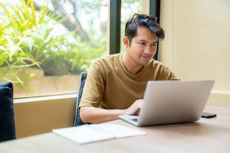 Asian freelance. Handsome asian man looking at device screen and smiling enjoy remote work. freelance concept.の写真素材