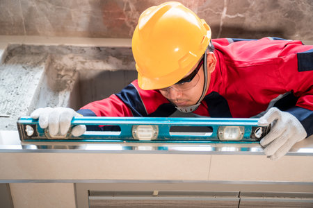An engineer or inspector wearing a safety gear is using a water level to inspect the construction of...