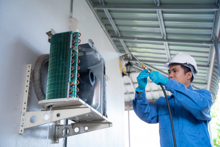 Air conditioner technician wearing a safety suit uses a high-pressure water jet to clean the air conditioner to clear the dust on the air conditioner.の写真素材