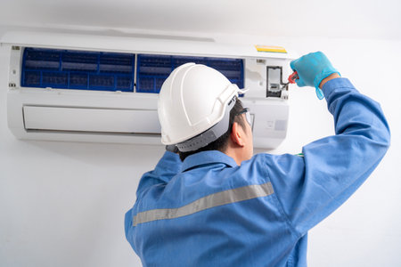 Air technician man repairing and installs air conditioner on white wall. Service concept of an air conditioner technician.の写真素材