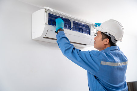 Air technician wearing blue uniform service checking and repairing air conditioner on white wall. Service concept of an air conditioner technician.の写真素材