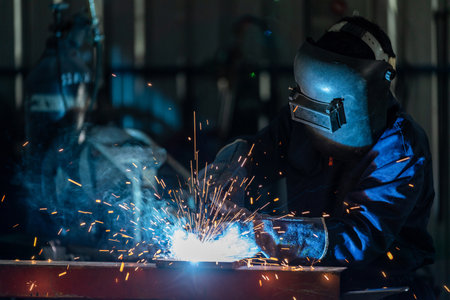 Asian workers wearing industrial uniforms and welded iron mask at steel welding plants. heavy industrial worker inside factory with industrial worker using welding machine.の写真素材