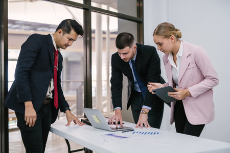 Group of diverse businesspeople working together on a laptop in a modern workplace.の写真素材
