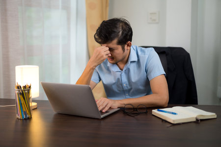 A men having migraine Headaches due to long hours working and booking laptops at home desks.の写真素材