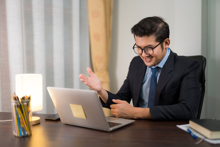 Happy young businessman sitting and discussing online meeting with laptop in private office.の写真素材