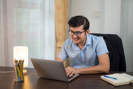 Asian young men in glasses is using laptop working at desk happily at home.の写真素材