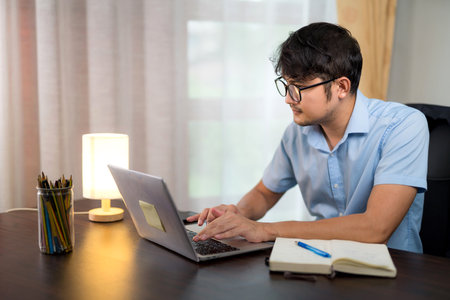 Asian handsome man in glasses working on desk with laptop at home.の写真素材