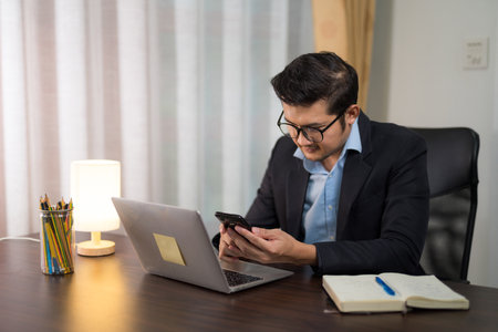 Asian businessman using smart phone on desk with laptop at home.の写真素材