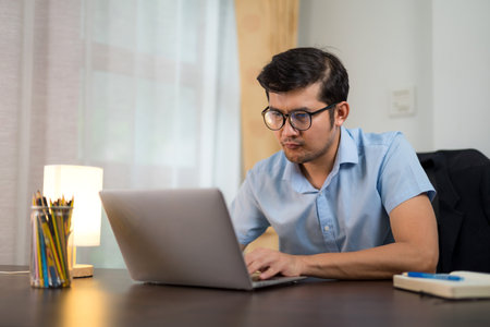 Asian young men in glasses are serious about working with laptops. via online from home.の写真素材