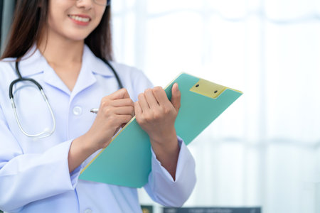 Close up of Asian beautiful female doctor in white coat with stethoscope  holding chart sheet , waist up. Medical student. Medical concept.の写真素材