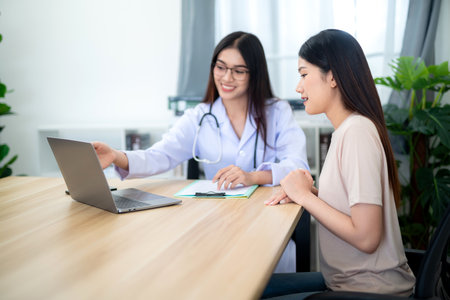 Asian female doctor consulting patient or client while looking at treatment guidelines on laptop with medical technology at the clinic. Health care concept. selective focus on patient.の写真素材