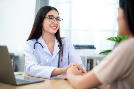 Beautiful female doctor holding female patient's hand to encourage medical treatment and health care at clinic. Health care concept.の写真素材