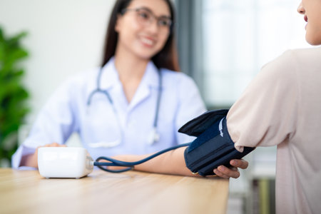 Close up hand of A female doctor wearing armband for measuring blood pressure with digital sphygmomanometer to patient at hospital.の写真素材