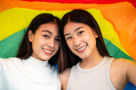 Smiling Asian couple looking at camera in rainbow flag protesting to show support. lesbian rainbow flag. Lesbian couple enjoy happy moments.の写真素材