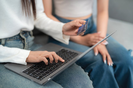 Two asian young women shopping online shopping on laptop with credit card while sitting together on sofa in living room. online shopping concept.の写真素材