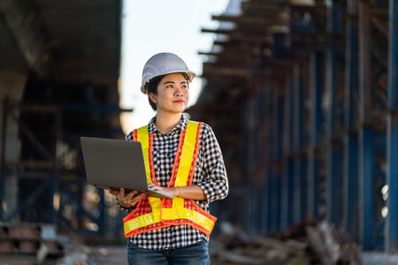 Smiling female engineer holding laptop at expressway construction site.の写真素材