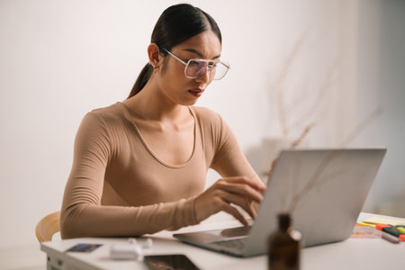 Asian male in eyeglasses and earphones using laptop computer while sitting at home office desk. LGBTの写真素材