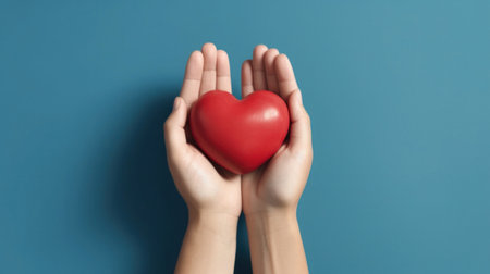 Hands holding a red heart on a blue background.の素材
