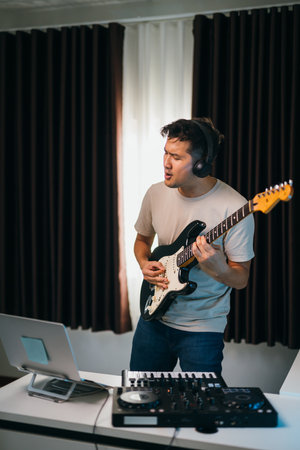 Asian male producer layering vocals over electronic beats, guitar and audio gear on the desk, in a modern and inspiring studio environment.の写真素材