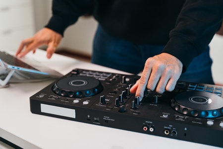 Close-up hands of a DJ seamlessly mixing tracks on a minimalist mixer console at a stylish home event.の写真素材
