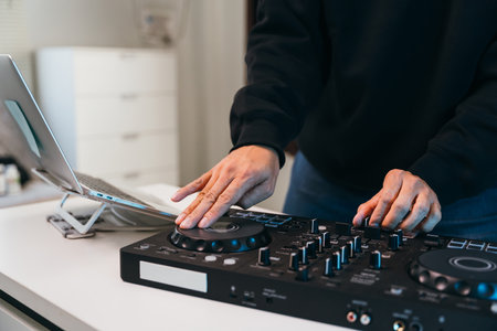 Close-up of hands adjusting knobs on a modern mixer console in a dark, lively club setting, glowing lights in the background.の写真素材