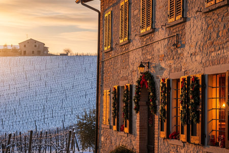 Traditional stone farmhouse adorned with Christmas garlands, wreaths, and red ribbons at sunset, surrounded by snowy vineyards in a winter countryside settingの素材