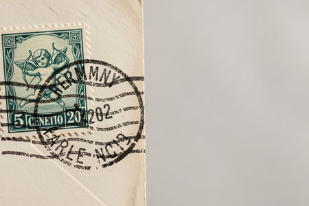 Macro close up of a vintage postage stamp featuring a Cupid illustration affixed to an aged envelope symbolizing love and sentiment.の素材