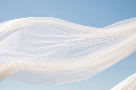 Wedding veil blowing in the wind against a clear blue sky showing the translucent white fabric creating an abstract shape.の素材