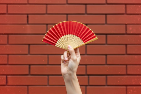 Vibrant silk fan against a red wall background showcases the cultural tradition of using decorative accessories.の素材