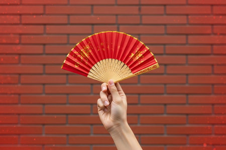 Traditional hand gesture holding a Chinese lunar fan is captured against the rough texture of the wall background.の素材