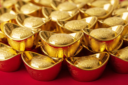 Vibrant gold ingots a seasonal symbol of fortune and money displayed on deep red velvet with rich shine and metallic luster.の素材