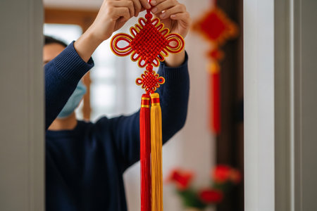 Decorating a doorway with hands carefully hanging a red and gold Chinese ornamental knot and silk tassel for the New Year reunion.の素材