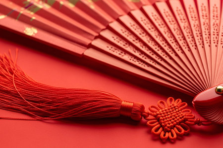Oriental folding fan with a long detailed tassel and subtle gold accent a vibrant red silk paper cultural tradition ornamental element close up.の素材