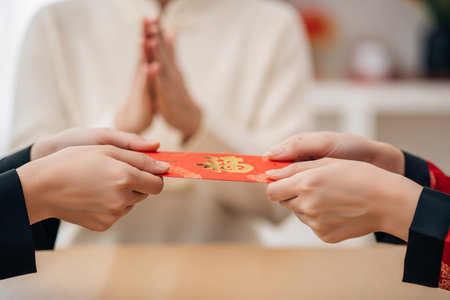 Traditional greeting ritual captured by hands wearing subtle silk cuffs presenting a red envelope symbolizing money and good fortune.の素材