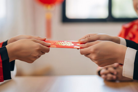 Family greeting with two pairs of hands exchanging a vibrant red money packet a traditional Chinese New Year ritual moment.の素材