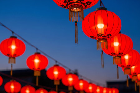 Ornamental paper lanterns in vibrant red hanging outdoors captured at twilight an atmospheric seasonal decorating element with high contrast colors.の素材
